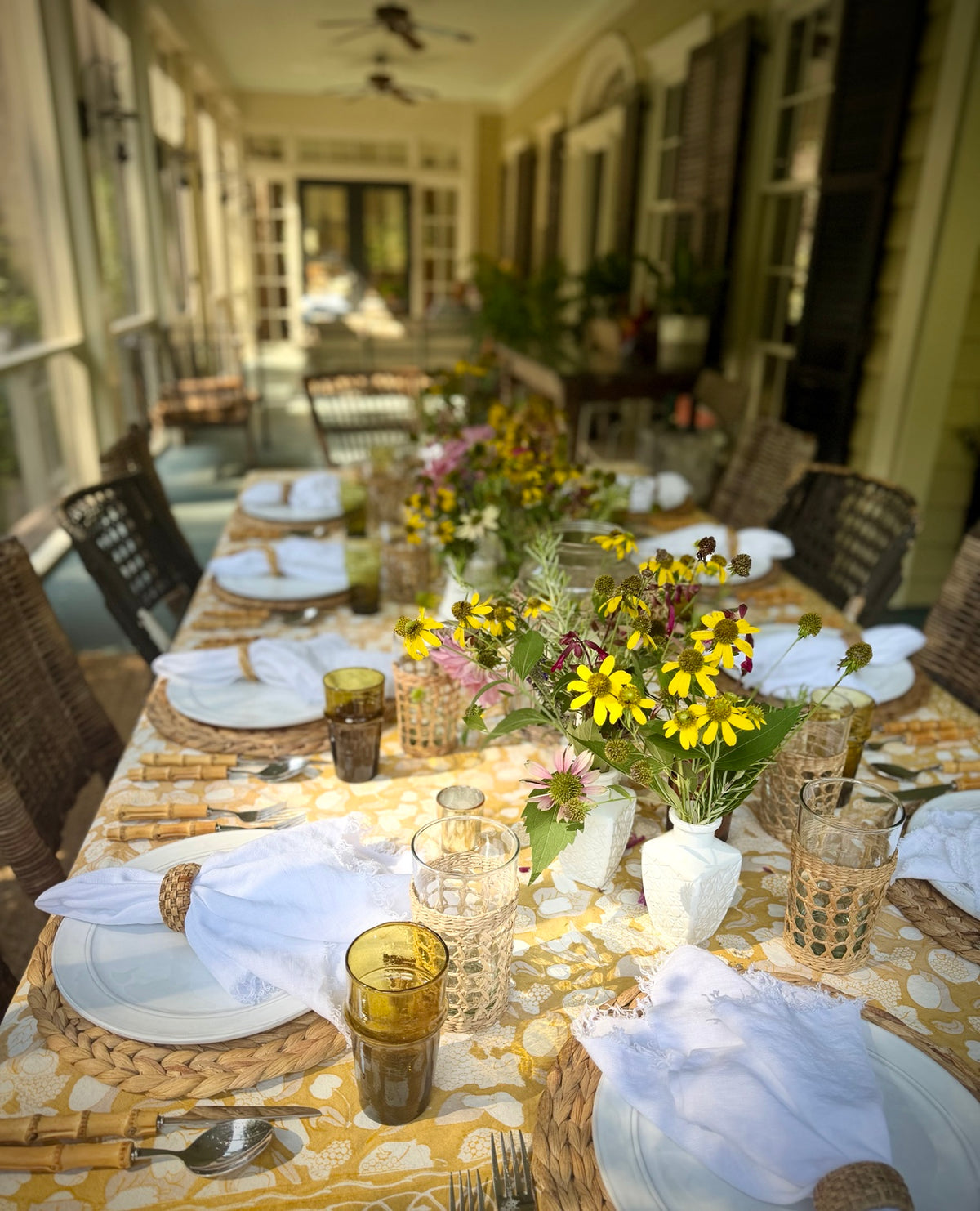 Fall table setting on a porch with woven placemats, amber glassware and garden flowers